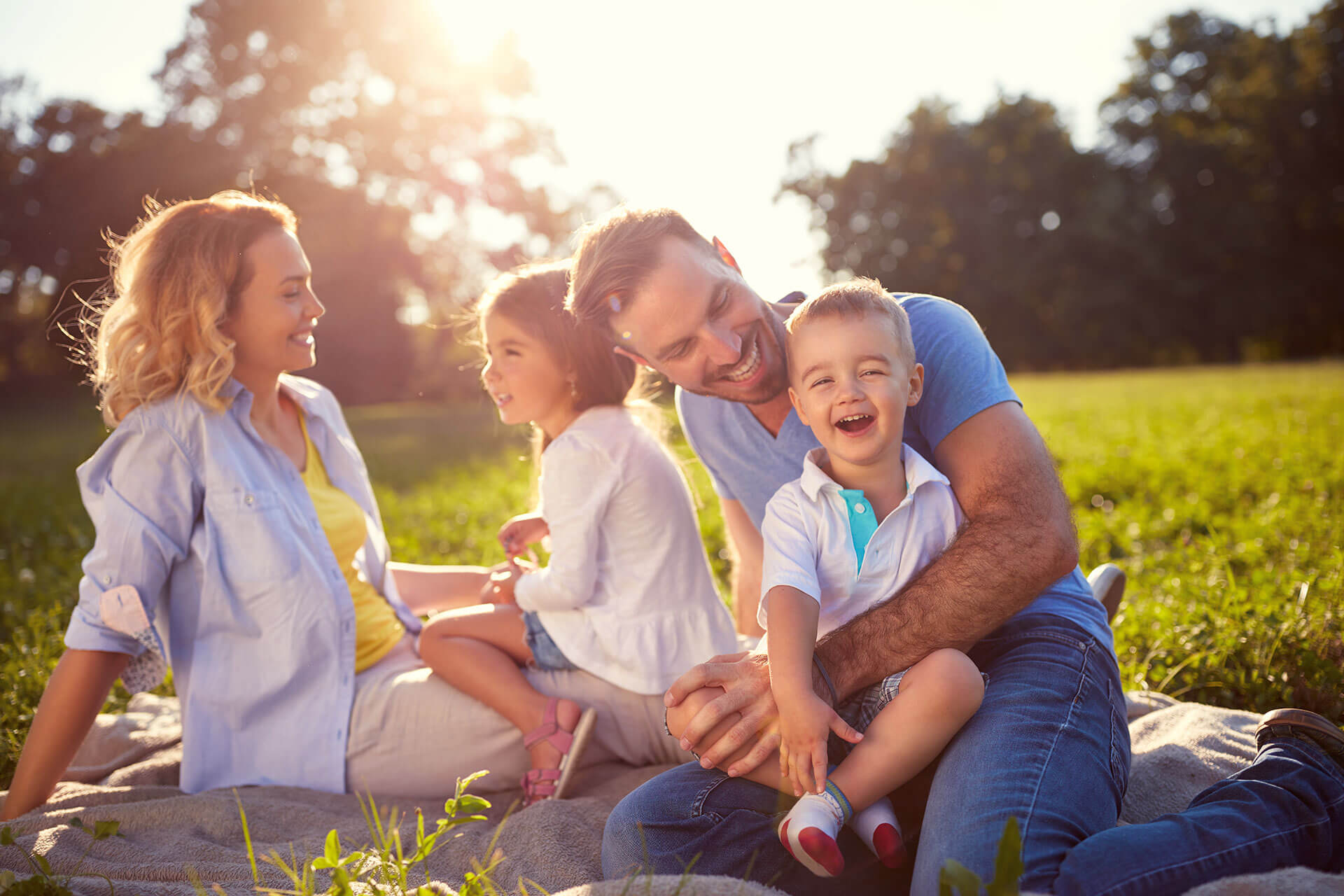 photo of a family sitting at a field with green trees background