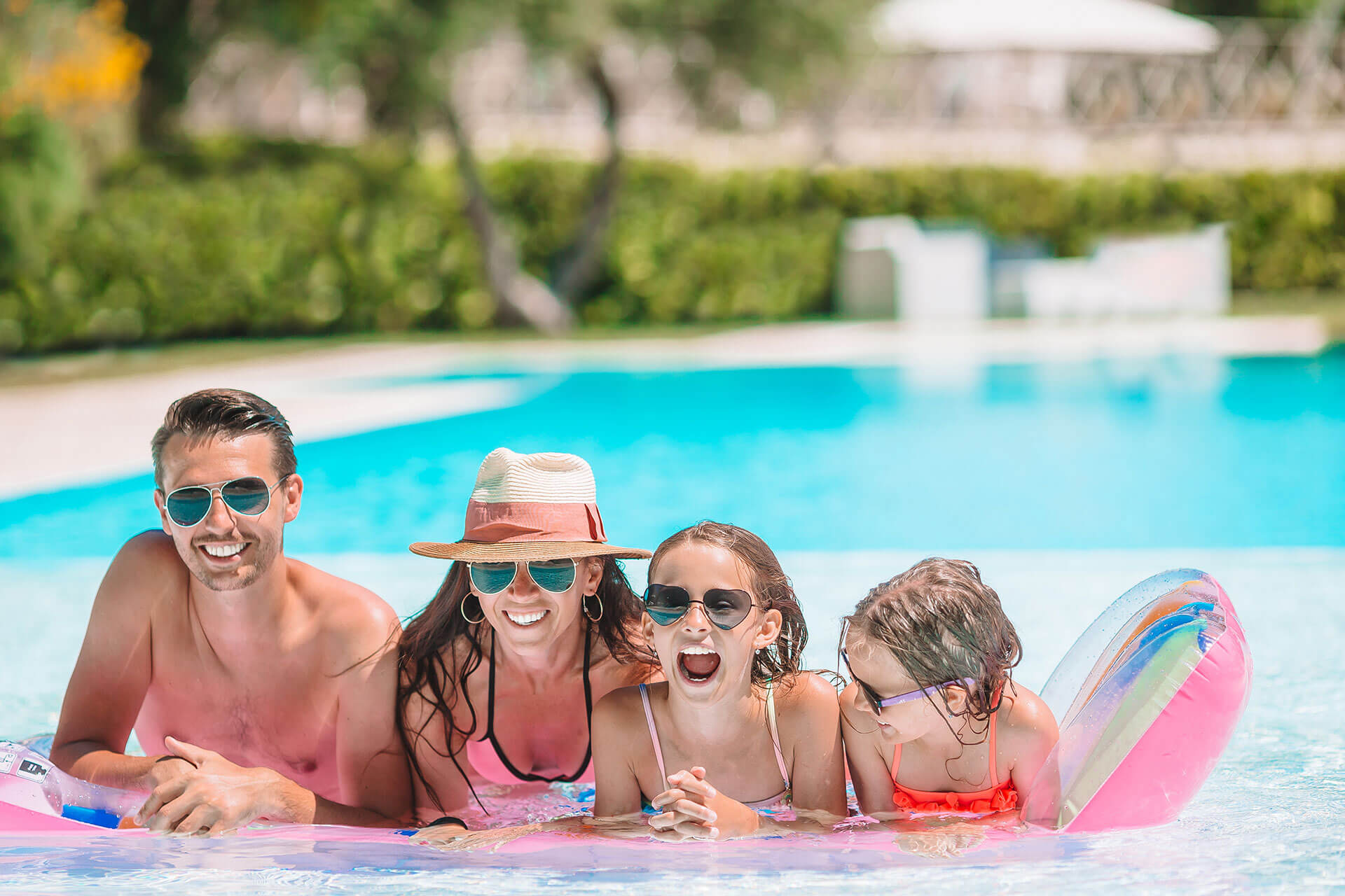 photo of a swimming pool with trees and a family of 4 with glasses inside the pool
